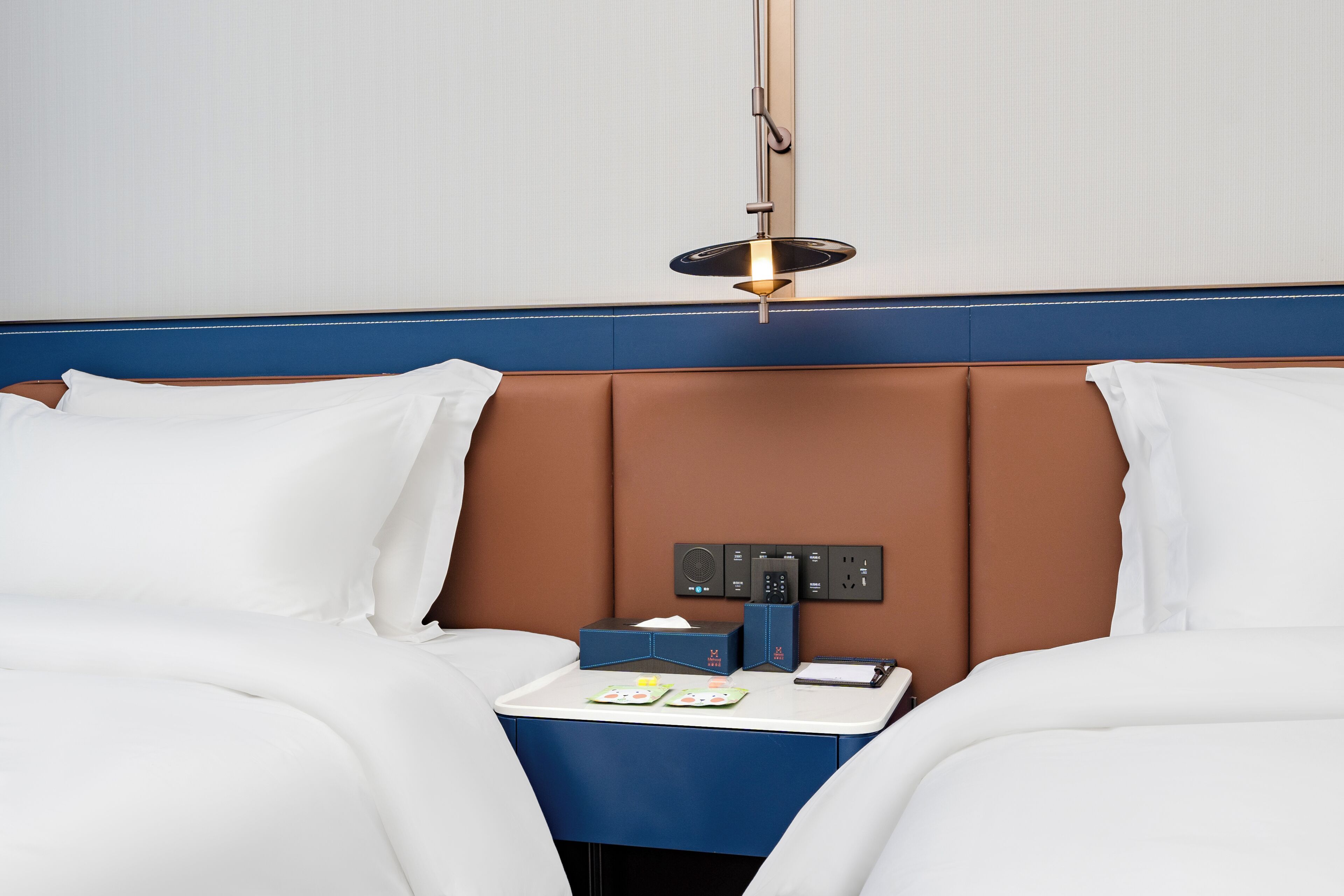 A hotel room with a bed, bedside table, lamp, and control panel.