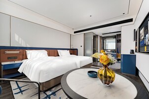 A hotel room with a bed, bedside table, and a round table with a vase.