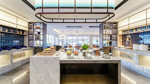 A modern hotel lobby with a marble reception desk, bookshelves, and a large window offering a view of the city.