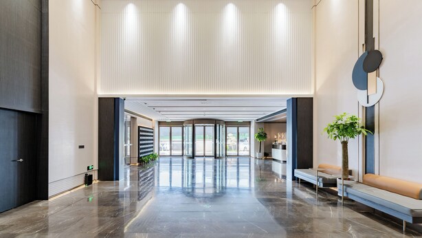 A spacious lobby with a marble floor, a reception desk, a seating area, and a large glass door entrance.