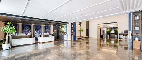 A spacious lobby with a reception desk, seating area, and a large plant.