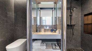 Un baño moderno con ducha envuelta en vidrio, inodoro y tocador con artículos de aseo.