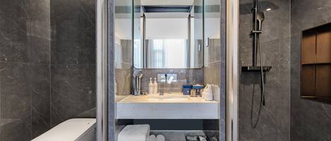 Un baño moderno con ducha envuelta en vidrio, inodoro y tocador con artículos de aseo.