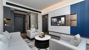 A modern hotel room with a sofa, a coffee table, a TV, and a large window.