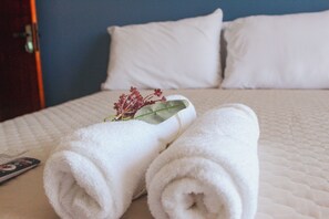 A neatly made bed with white linens, a remote control, and a decorative flower on the pillow. - Pousada Porto Maresias (Cabo Frio)