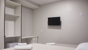 A hotel room with a bed, a TV mounted on the wall, a wardrobe, and a small bedside table. - Pousada Porto Maresias (Cabo Frio)
