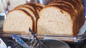 A loaf of bread in a clear plastic container with a serrated knife beside it. - Pousada Porto Maresias (Cabo Frio)