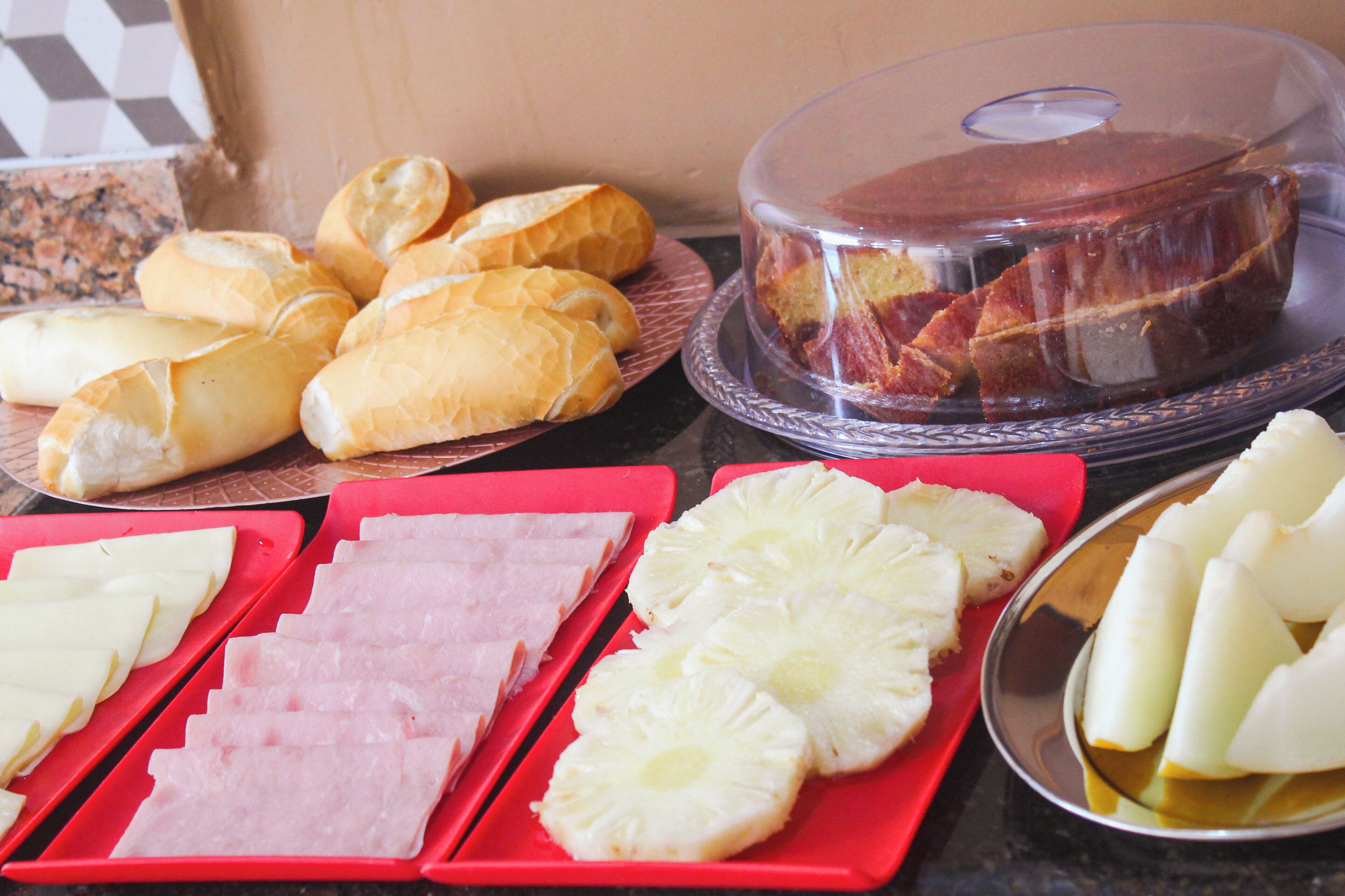 A buffet table with various food items including bread, ham, pineapple slices, and a covered cake.
