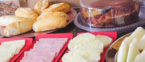 A buffet table with various food items including bread, ham, pineapple slices, and a covered cake.