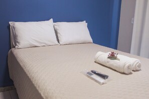 Habitación de hotel con cama, almohadas, una toalla enrollada con una flor y un control remoto.