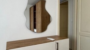 Ein Schlafzimmer mit einem Bett, einer Kommode mit Schubladen, einem Spiegel und einer Tür zu einem weiteren Raum.