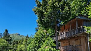Eine Holzhütte mit Balkon, umgeben von Bäumen und einem Berg im Hintergrund.