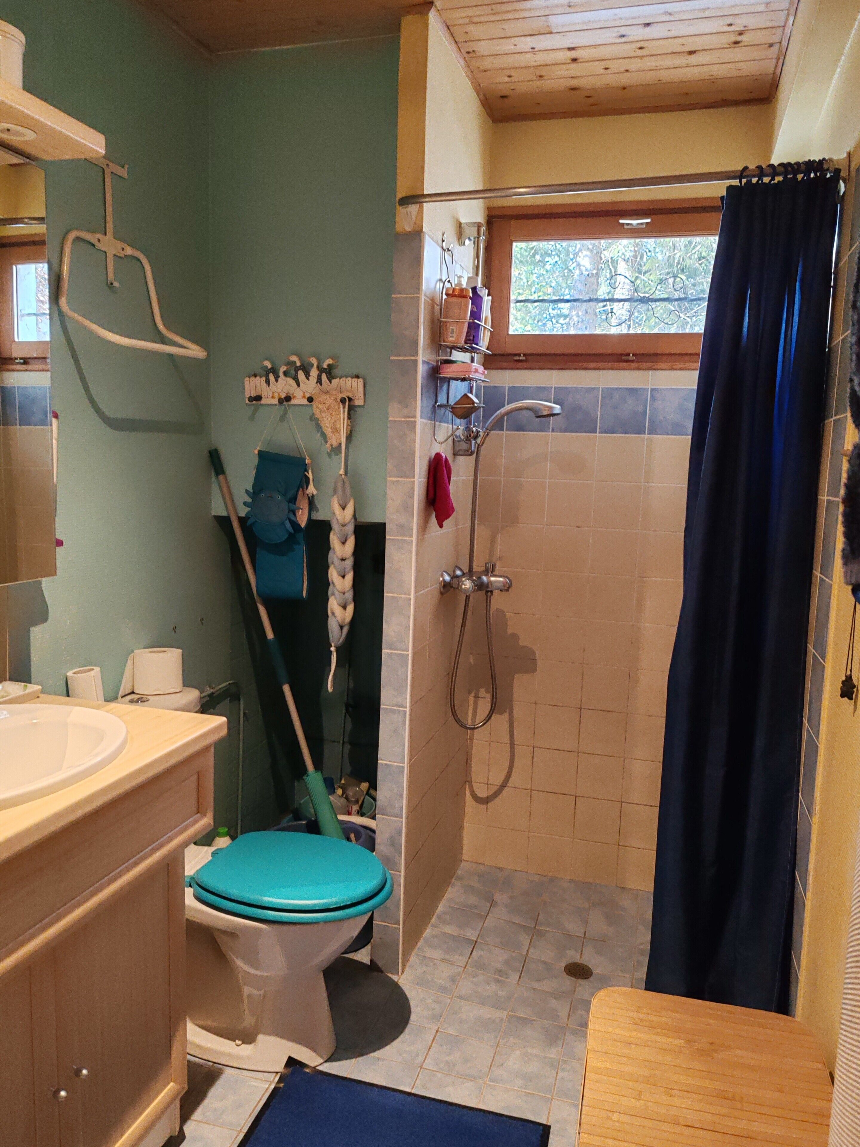 A bathroom with a toilet, sink, shower, and a mop leaning against the wall.