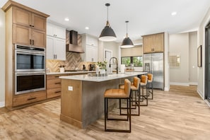 A modern kitchen with a central island, bar stools, stainless steel appliances, and pendant lighting.