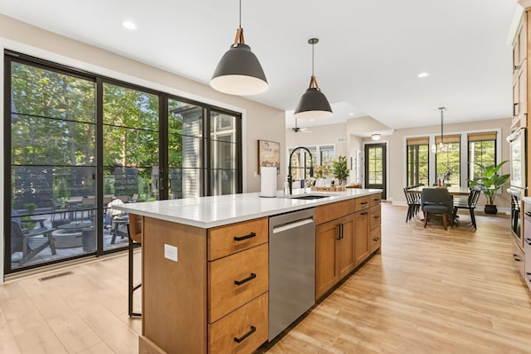 A modern kitchen with a large island, wooden cabinets, and pendant lighting.