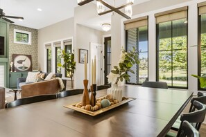 A dining area with a long table, chairs, a chandelier, and a view of the outdoors.