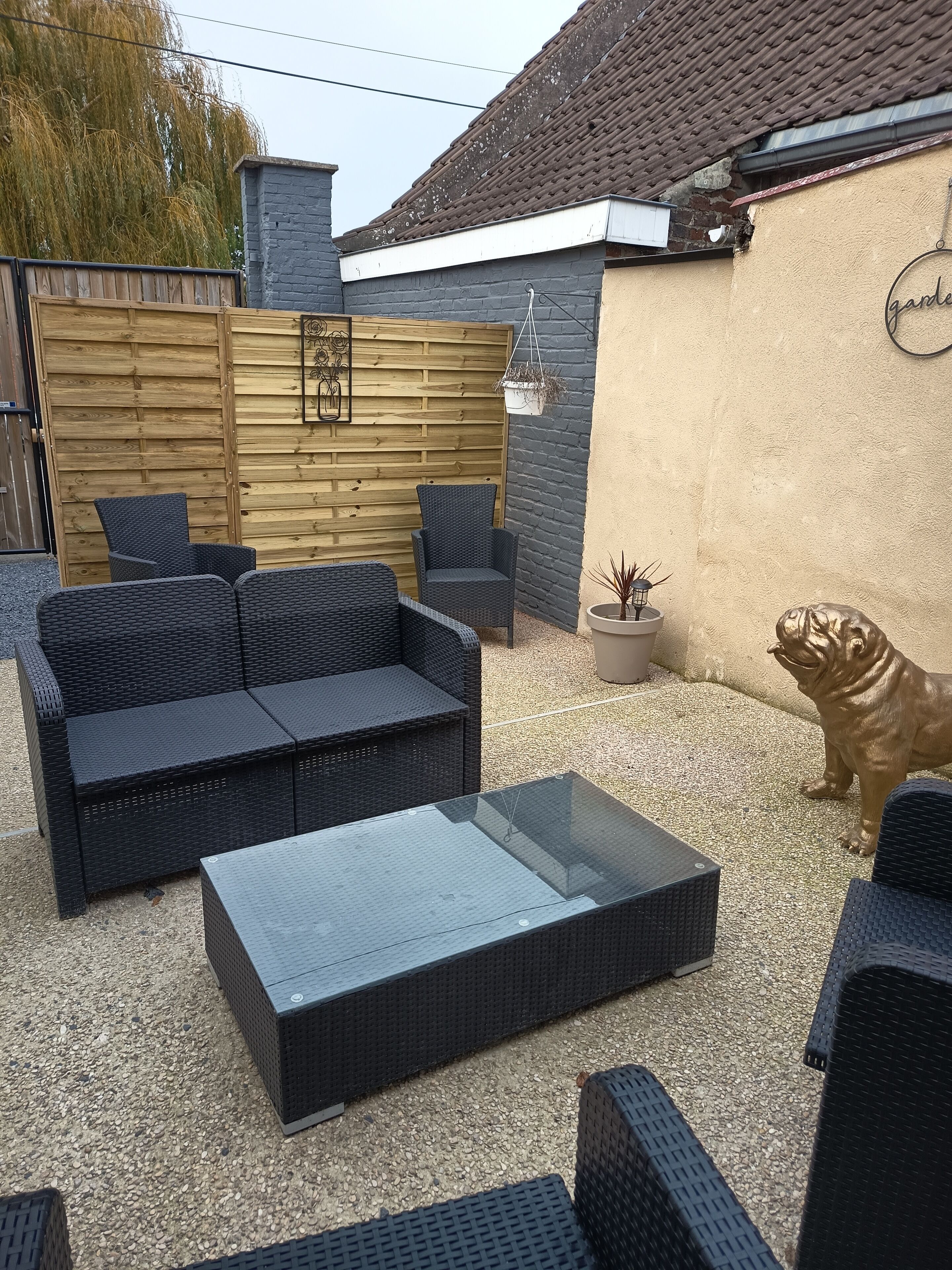 A patio area with a black wicker sofa, a glass-top coffee table, and a decorative dog statue.