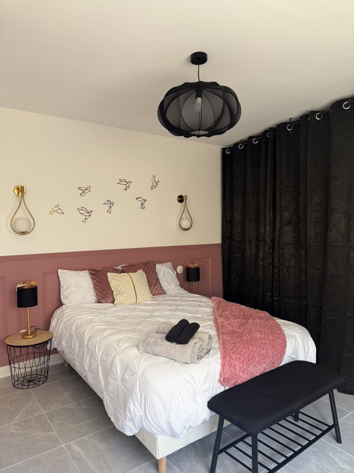 Un dormitorio ordenado con una cama grande, lámparas de noche, un banco y decoración en la pared.