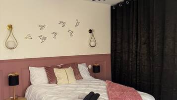Un dormitorio ordenado con una cama grande, lámparas de noche, un banco y decoración en la pared.