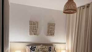 Une chambre à coucher comprenant un lit, deux tables de chevet, un luminaire suspendu et une œuvre d’art fixée au mur.