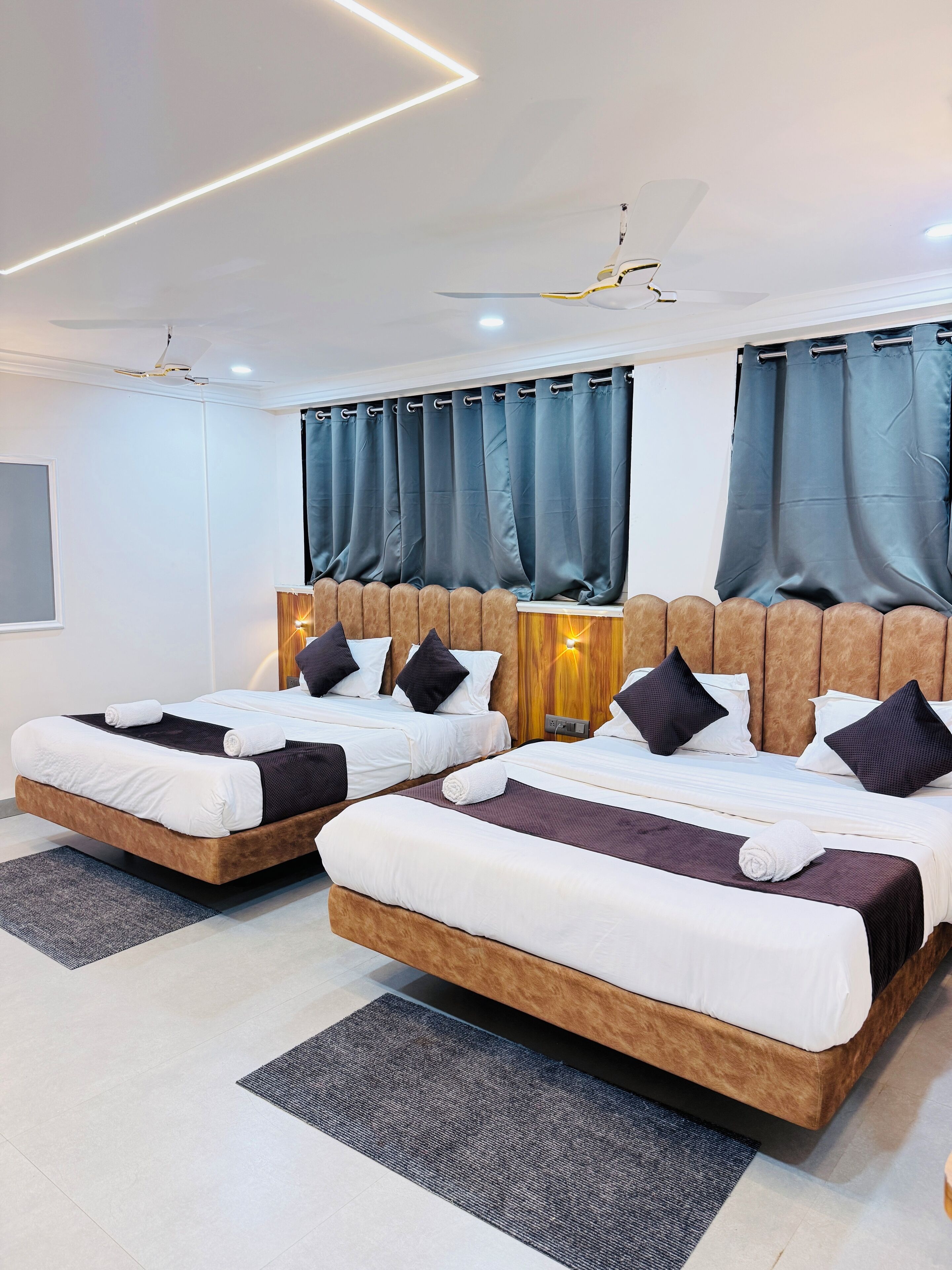 A modern hotel room with two beds, a ceiling fan, and a large window with curtains.