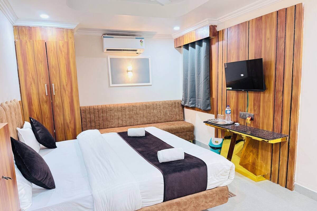 Ein Hotelzimmer mit einem Bett, einem an der Wand befestigten Fernseher, einem kleinen Tisch mit einer Wasserflasche und einem Holzschrank.