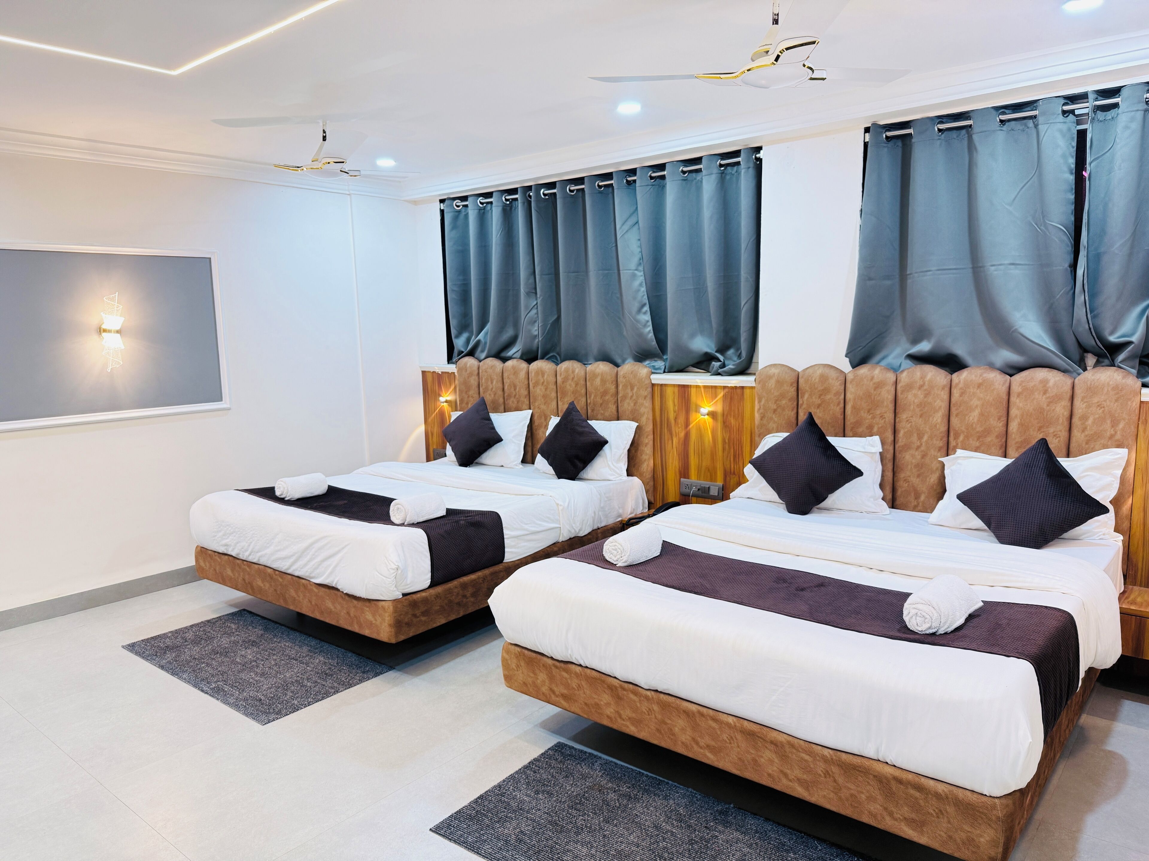 Moderni hotellihuone, jossa on kaksi sänkyä, suuri peili ja kattotuuletin.