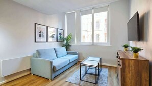 Ein Wohnzimmer mit einem hellblauen Sofa, einem kleinen Couchtisch, einem Holzschrank und einem an der Wand befestigten Flachbildfernseher.