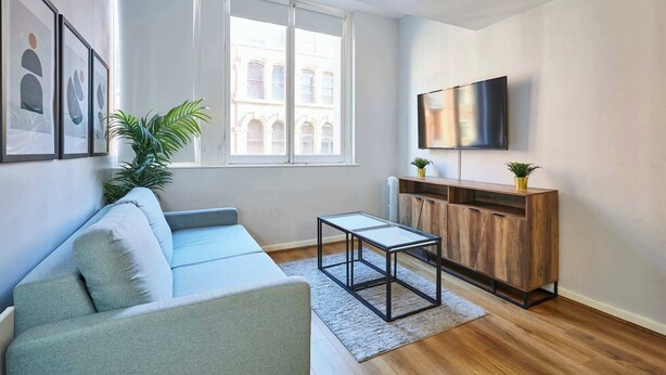 Ein modernes Wohnzimmer mit einer Couch, einem Couchtisch, einem Fernseher und einem Fenster mit Blick auf Gebäude.