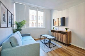 A modern living room with a sofa, a coffee table, a TV, and a window with a view of buildings. - Host & Stay | Apartment 1, Stanley Street (Liverpool)
