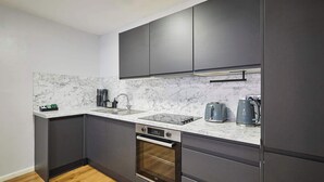 Eine moderne Küche mit dunklen Schränken, einer Marmorarbeitsplatte, einem eingebauten Backofen und einer Kaffeemaschine.