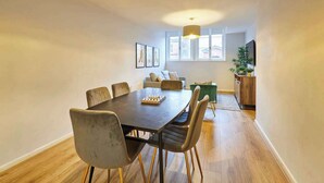Un coin repas avec une table et des chaises en bois, un canapé, un téléviseur et une plante.