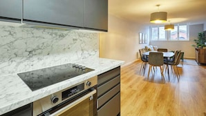 Une cuisine moderne dotée d’un plan de travail en marbre, d’un four encastré et d’un coin repas avec une table et des chaises en bois.
