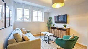 Un salon moderne avec un canapé, un fauteuil vert, une table basse et un téléviseur fixé au mur.