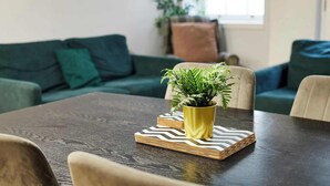 Un tavolo da pranzo con una pianta in vaso giallo, un sottopiatti a motivi a spina di pesce e una pila di libri.
