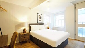 Una camera da letto moderna con un letto grande, un comodino in legno, una sedia e un quadro appeso alla parete.