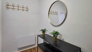Een kamer met een zwarte console tafel, twee potplanten, een spiegel met gouden lijst en een kapstok met haken.