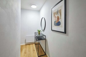 Ein Flur mit Holzboden, einem schwarzen Metall-Konsolentisch, einer kleinen Pflanze, einem runden Spiegel und einem gerahmten abstrakten Gemälde an der Wand.