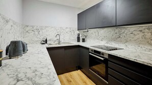 Una cocina compacta con armarios oscuros, encimera de mármol y horno empotrado.