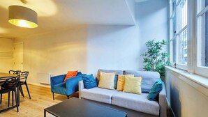 Una sala moderna con un sofá gris, una mesa de centro negra y una zona de comedor con una mesa y sillas. Hay un ventanal con vistas al exterior.