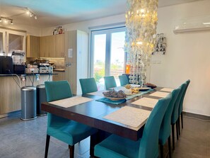 A modern dining area with a dark wooden table, teal upholstered chairs, and a decorative glass chandelier. - Room-sea View Oasis, Beach, Pool, Gym (Oroklini)