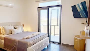A hotel room with a bed, a TV, a balcony, and a wooden side table.