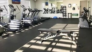 Een sportschool met loopbanden, elliptische trainers en een bankje.
