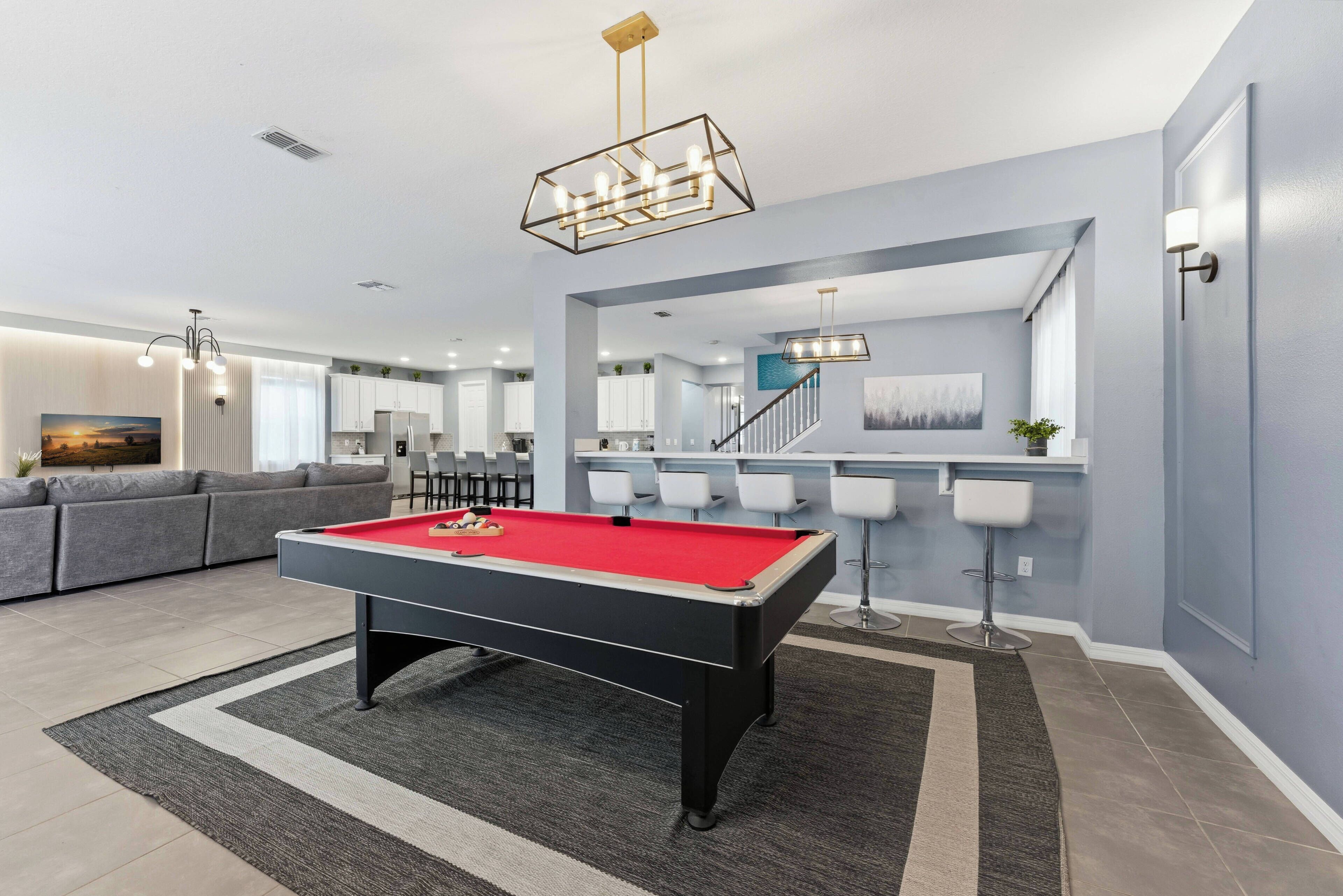 Een moderne woonkamer met een pooltafel, grijze banken en een trap naar een eetgedeelte.