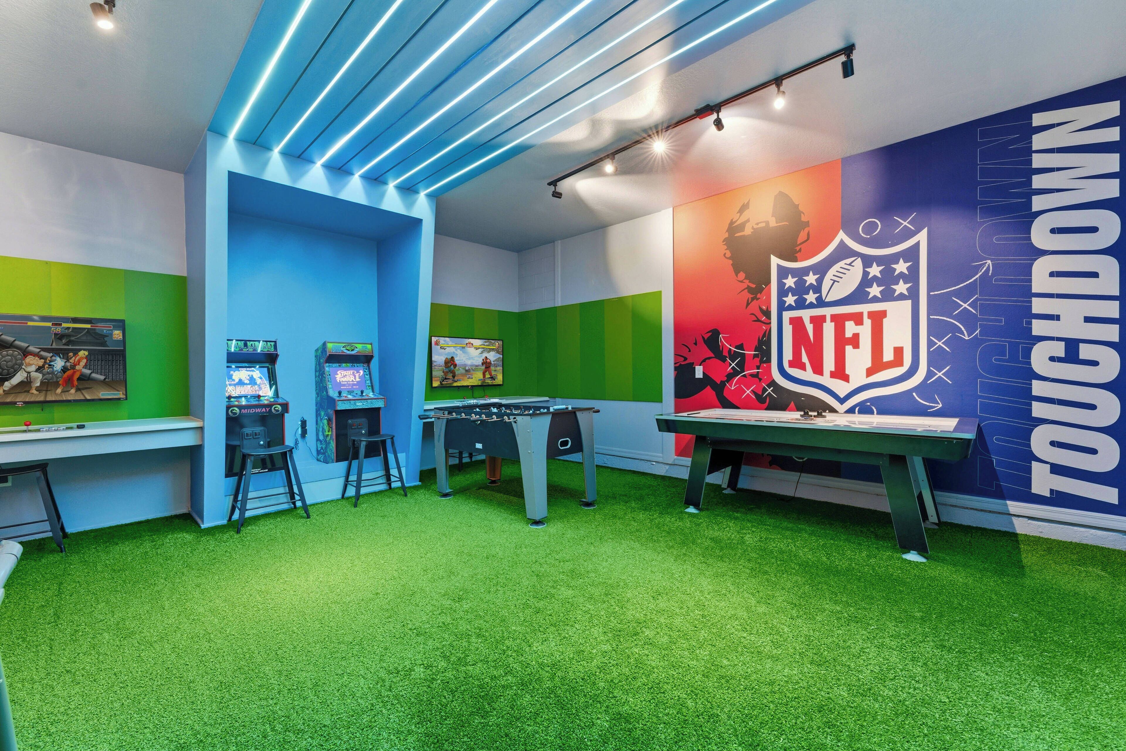 A room with green artificial turf, two foosball tables, and two arcade machines.