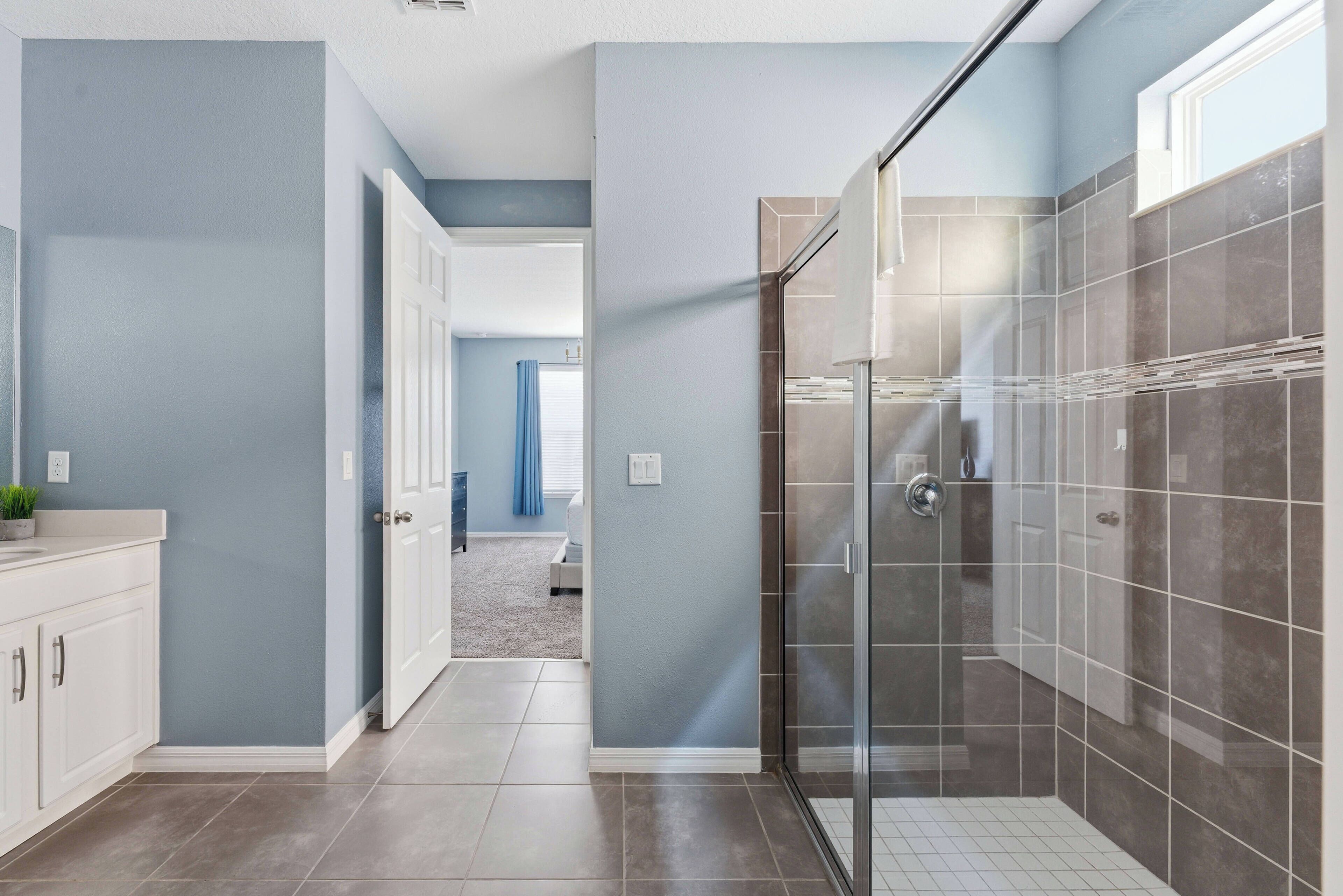 A modern bathroom with a glass shower enclosure, a white vanity, and a visible door leading to another room.