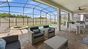 Eine überdachte Außenveranda mit Pool, Korbmöbeln und Grillplatz.