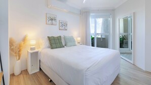 Een moderne slaapkamer met een groot bed, nachtkastjes met lampen en uitzicht op het groen via een schuifdeur.