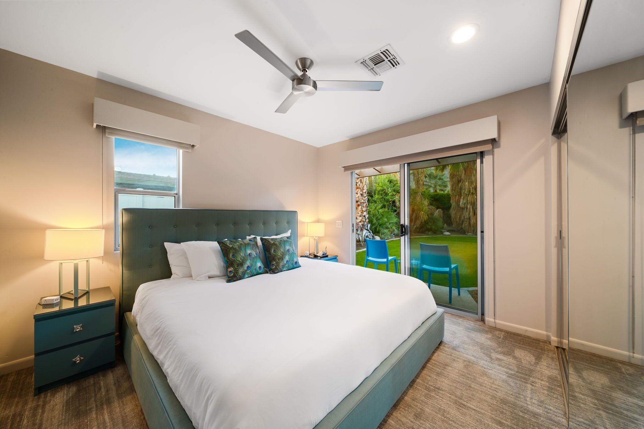 A bedroom with a bed, nightstands, a ceiling fan, and a sliding glass door leading to a balcony.