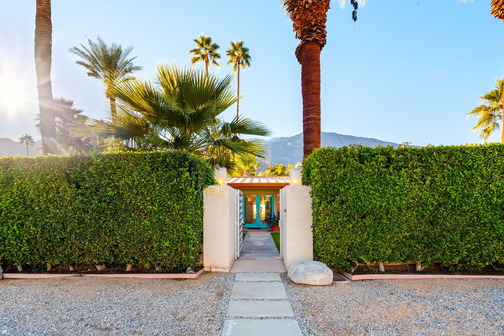 A pathway leading to a building with the number 1515, surrounded by lush greenery and palm trees.